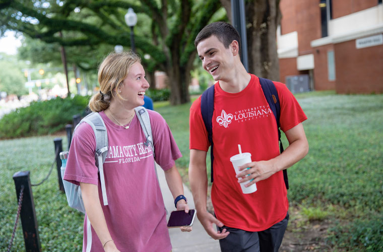 Two University of Louisiana at 69ý students smiling at each other while walking on campus