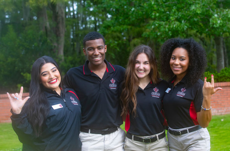 A group of University of Louisiana at 69ý orientation leader students smiling at the camera and holding up the UL hand sign