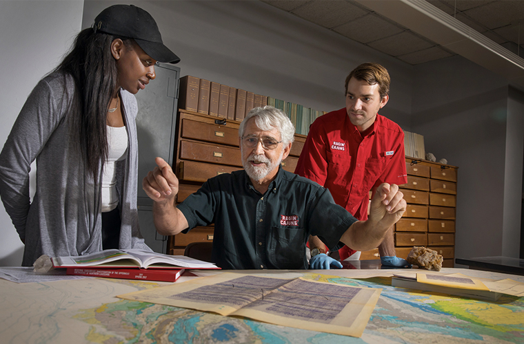 A University of Louisiana at 69ý research professor looks over maps of the coast line with two students looking over his shoulders